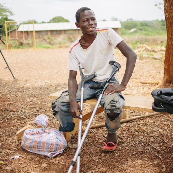 A Central African man with one leg sits on a bench while holding crutches.