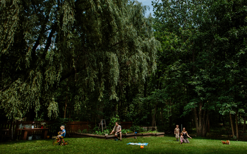A family in a yardshaded by trees with a garden and chickens.