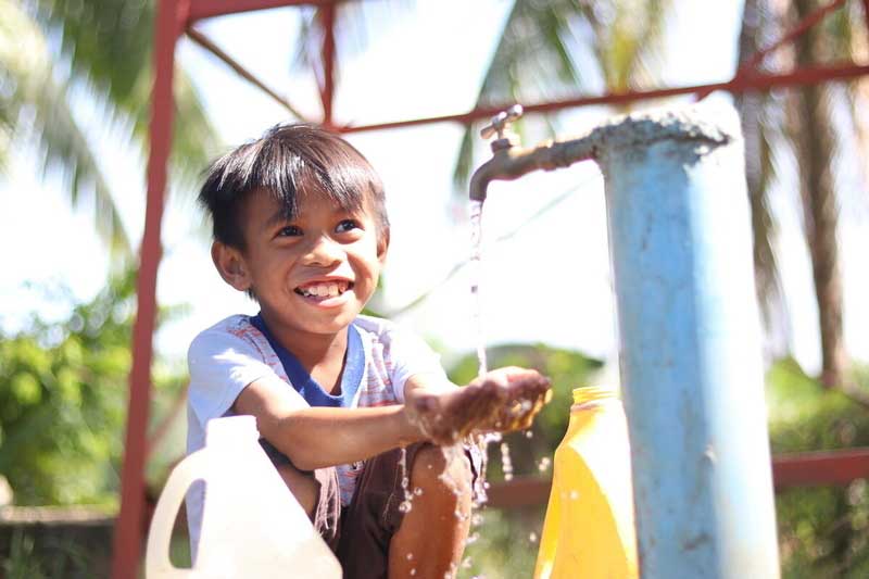 A little boy from the Philippines smile washing his hands