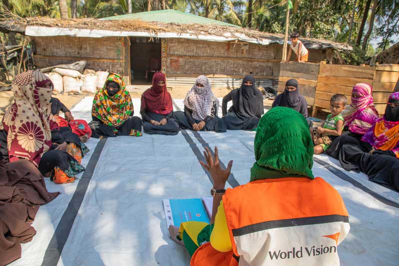 World Vision staff member in Bangladesh sits facing a circle of women sharing in a discussion.