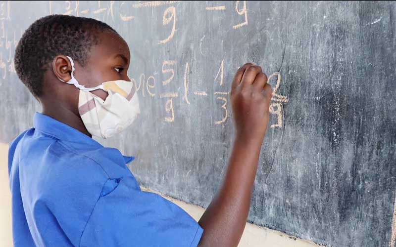 A boy wearing a blue school uniform solves a math equation on a chalkboard.
