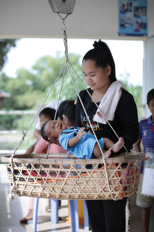 A young mom places her baby inside a straw basket to be weighed.
