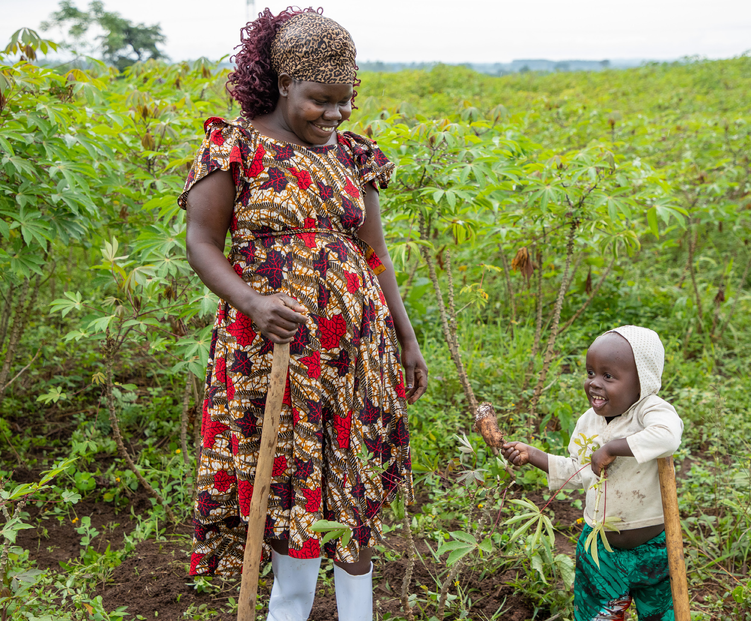 A mother looks at her child holding food in a green field.