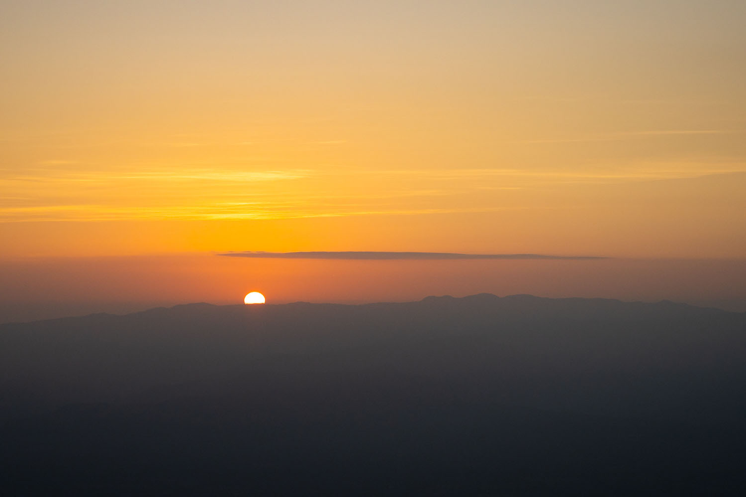 The sun peeks out from the horizon line over Rift Valley in Kenya. 
