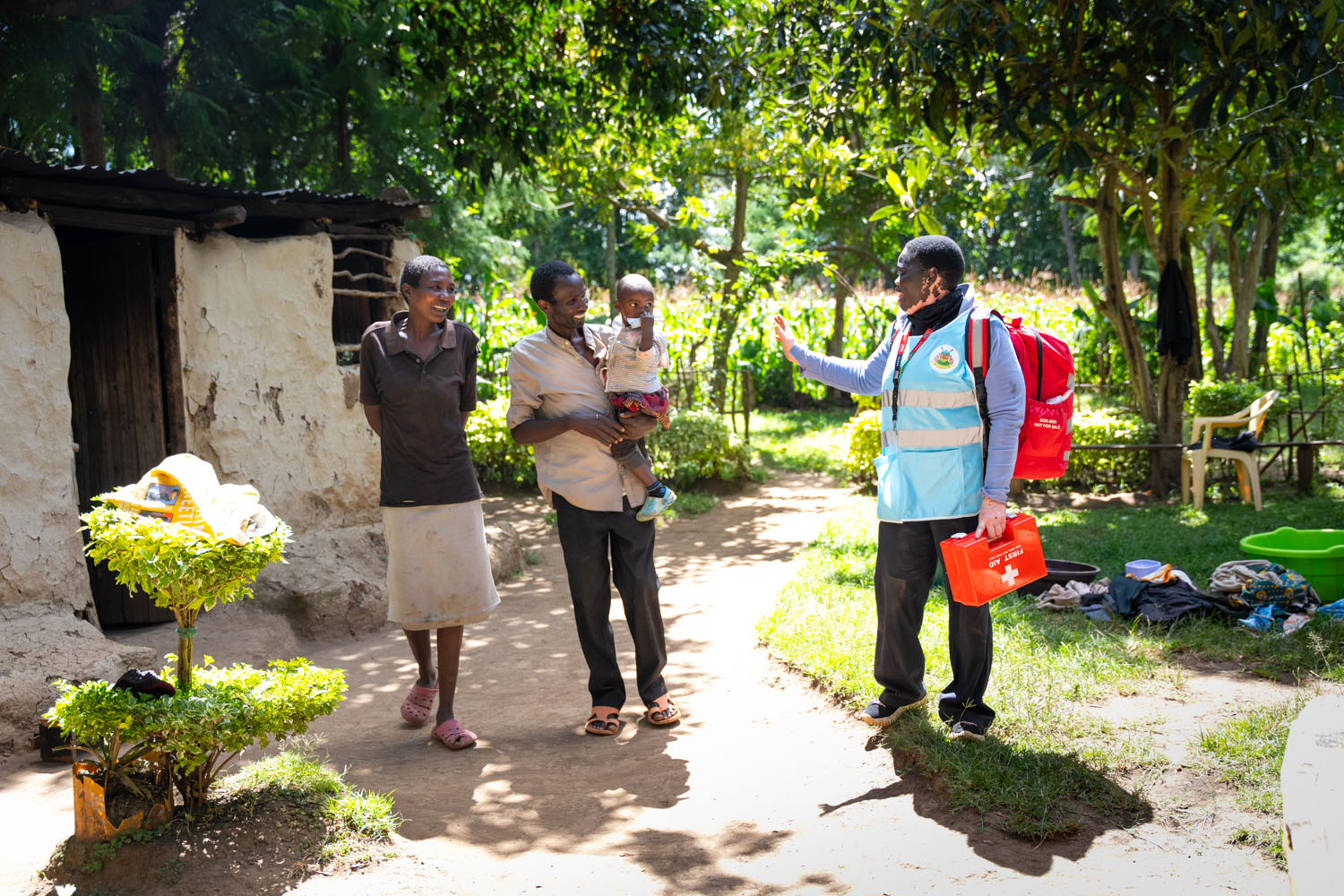 A Kenyan medical staff carrying a first aid kit talks to a man carrying his child and standing beside his wife. 