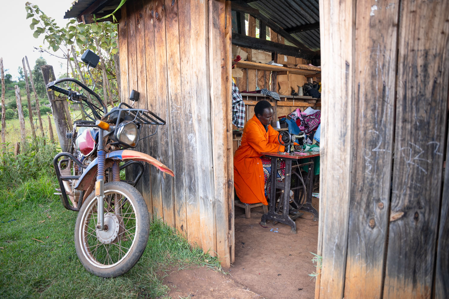 A Kenyan woman wearing an orange dress works at her sewing machine inside her home. 