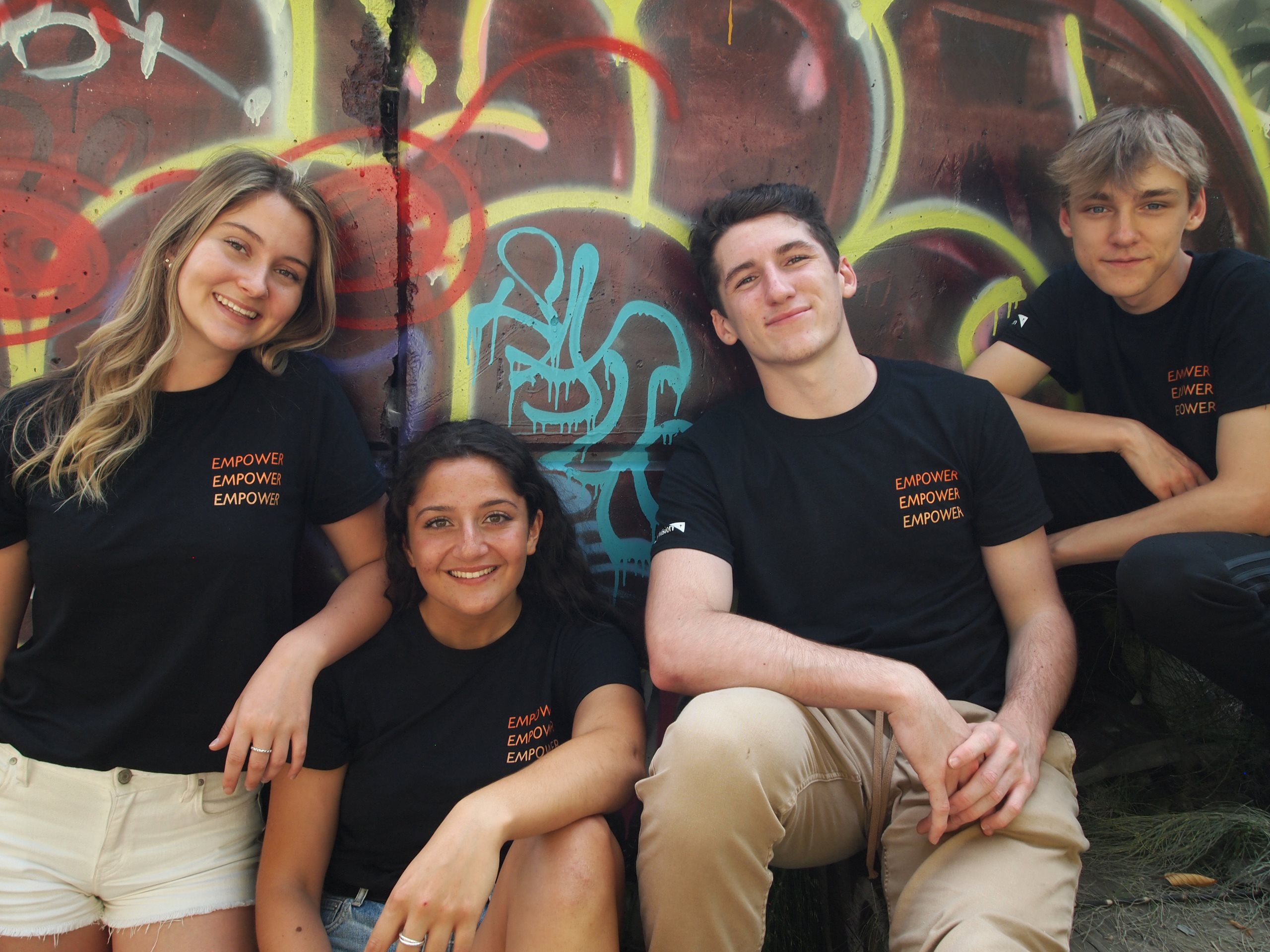 Four young people, two women and two men, smile at the camera, wearing World Vision t-shirts that say "Empower" on them.