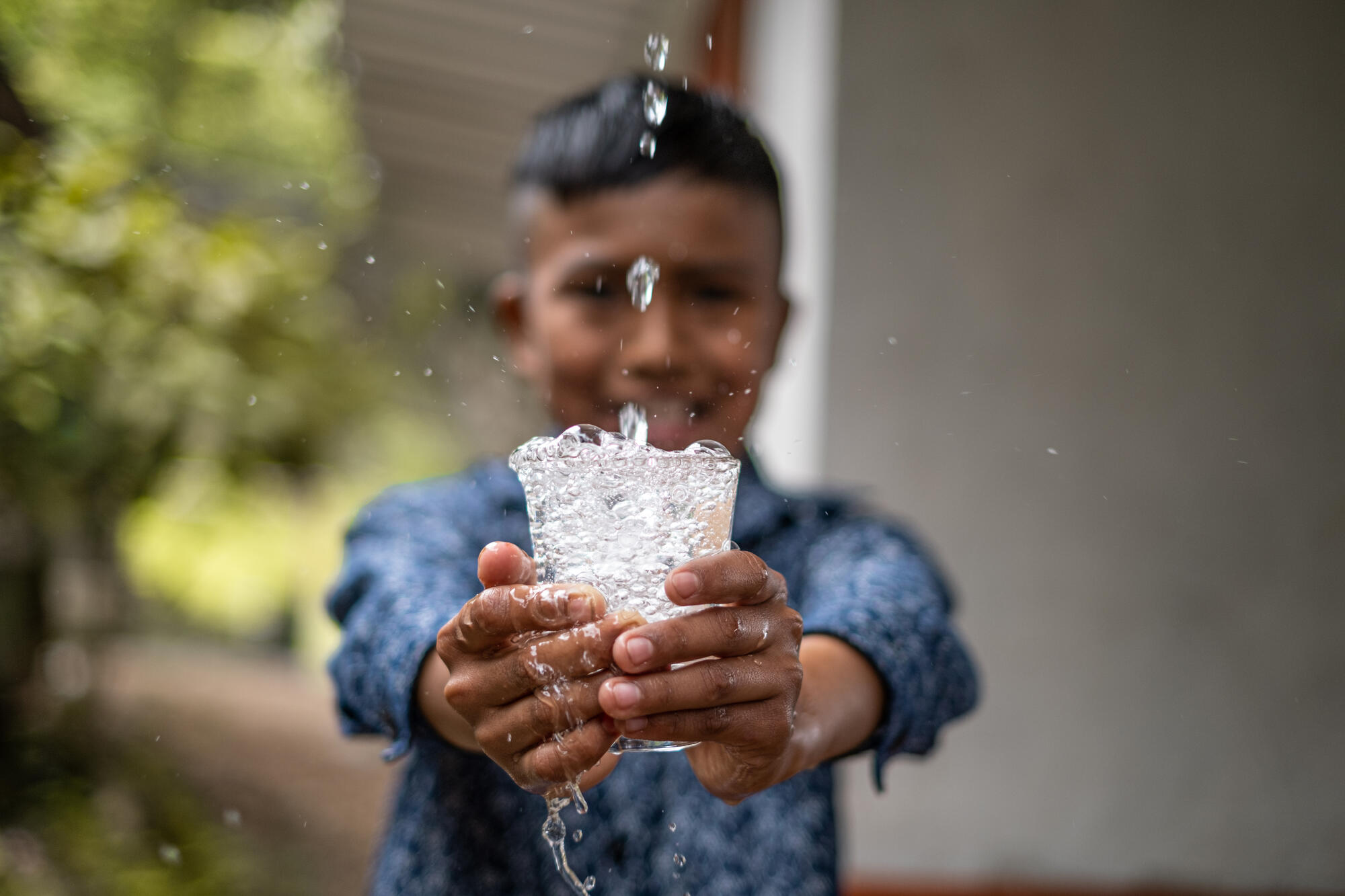 A young boy holds a glass of splashing water.