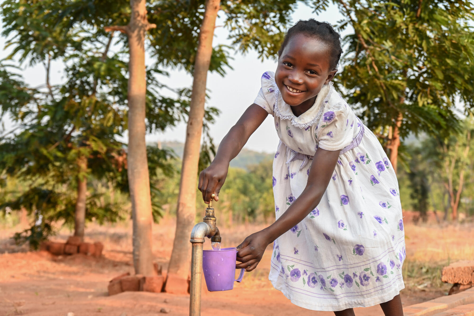 Young smiling girl pours water from a water point into a cup.