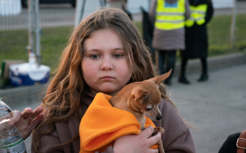 A young girl holds her dog, staring off into space.