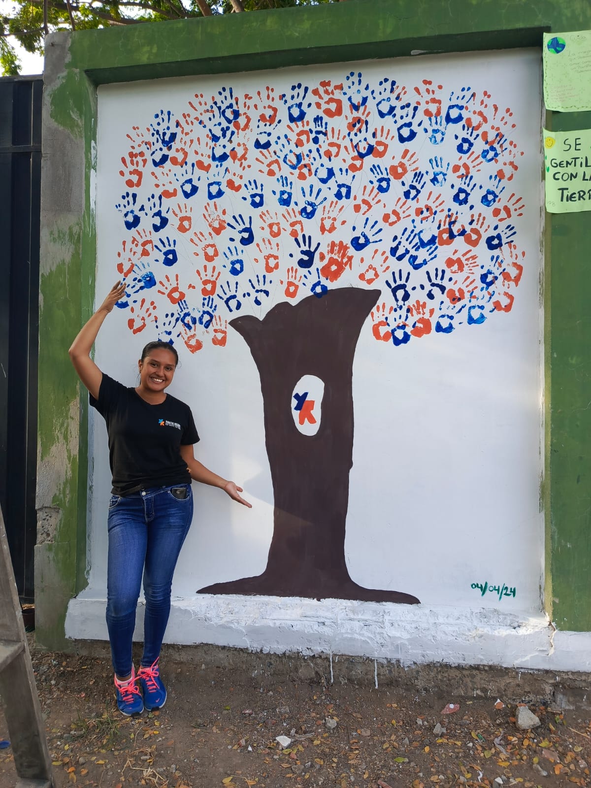 A young woman shows a tree painted on a mural with the hands of the participants of the Youth Ready program.