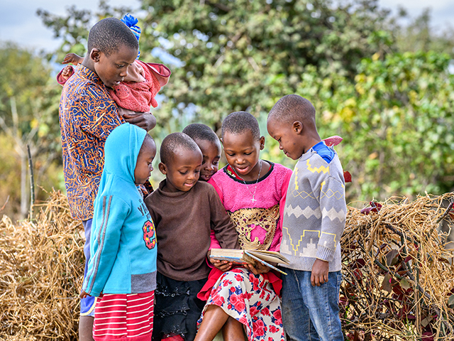 Three happy children stand together and smile at the camera.