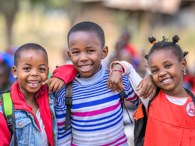 Three happy children stand together and smile at the camera.