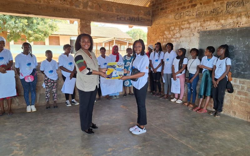 A girl in a white t-shirt hands an action plan to a female service provider wearing a brown vest and striped shirt.