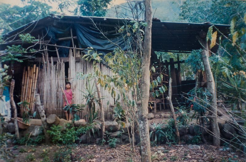 A young boy from El Salvador stand at the door of a wooden hut