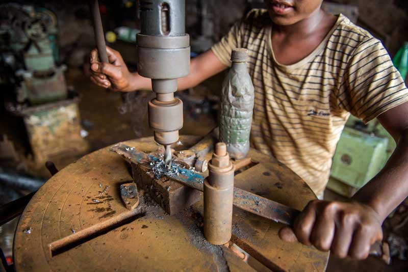 Close up of a boy's hands working with a machine at a workshop.