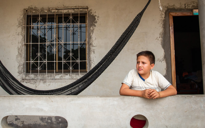 A boy stands besides a hammock in front of a house