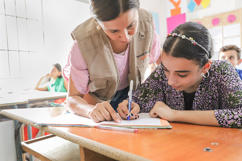 Une enseignante se penche au-dessus d’une étudiante pour l’aider dans ses travaux scolaires.