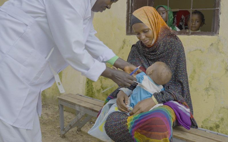 A doctor checks a Sudanese mother's child, cradled in her arms.
