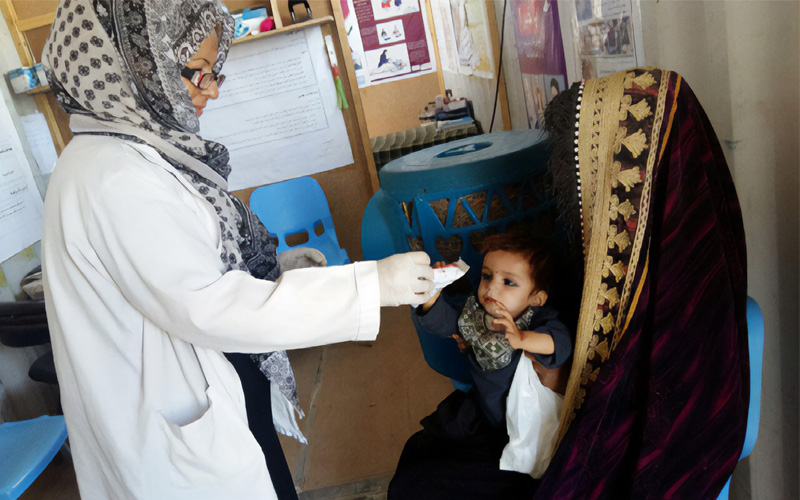 A mother is seated with her infant in a clinic as the child receives food from a nurse.