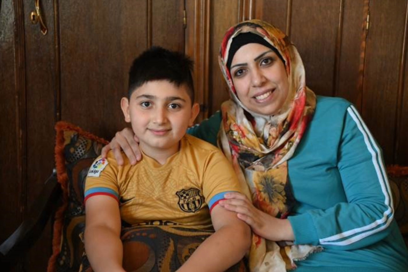 Smiling mother in headscarf with son in a soccer jersey.