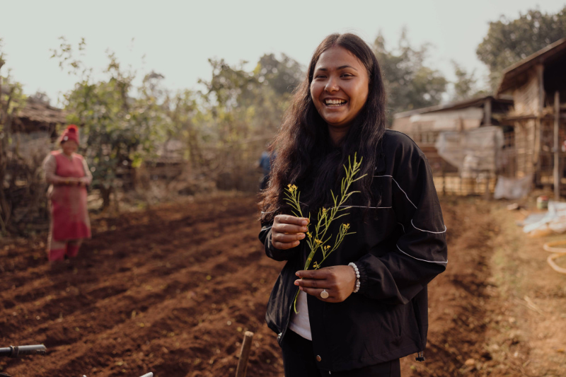 Smiling young woman holding sprigs of greenery in a freshly plowed field.