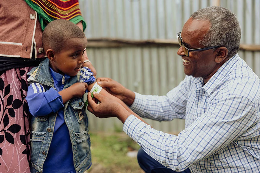 A health care worker provides care for Nuredin (left, blue shirt). Thanks to child sponsorship, he has overcome malnutrition and is thriving. (Ethiopia, 2023)