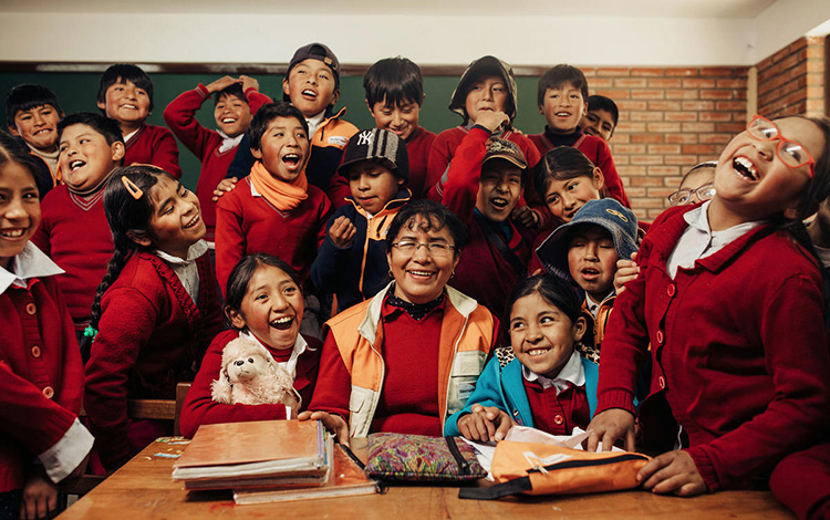 A woman sits with a group of school children in a classroom in Bolivia.